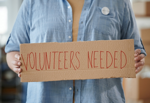 Man holding Volunteers Needed sign